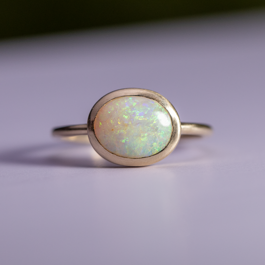 Gold ring with a greenish opal stone on a light purple background