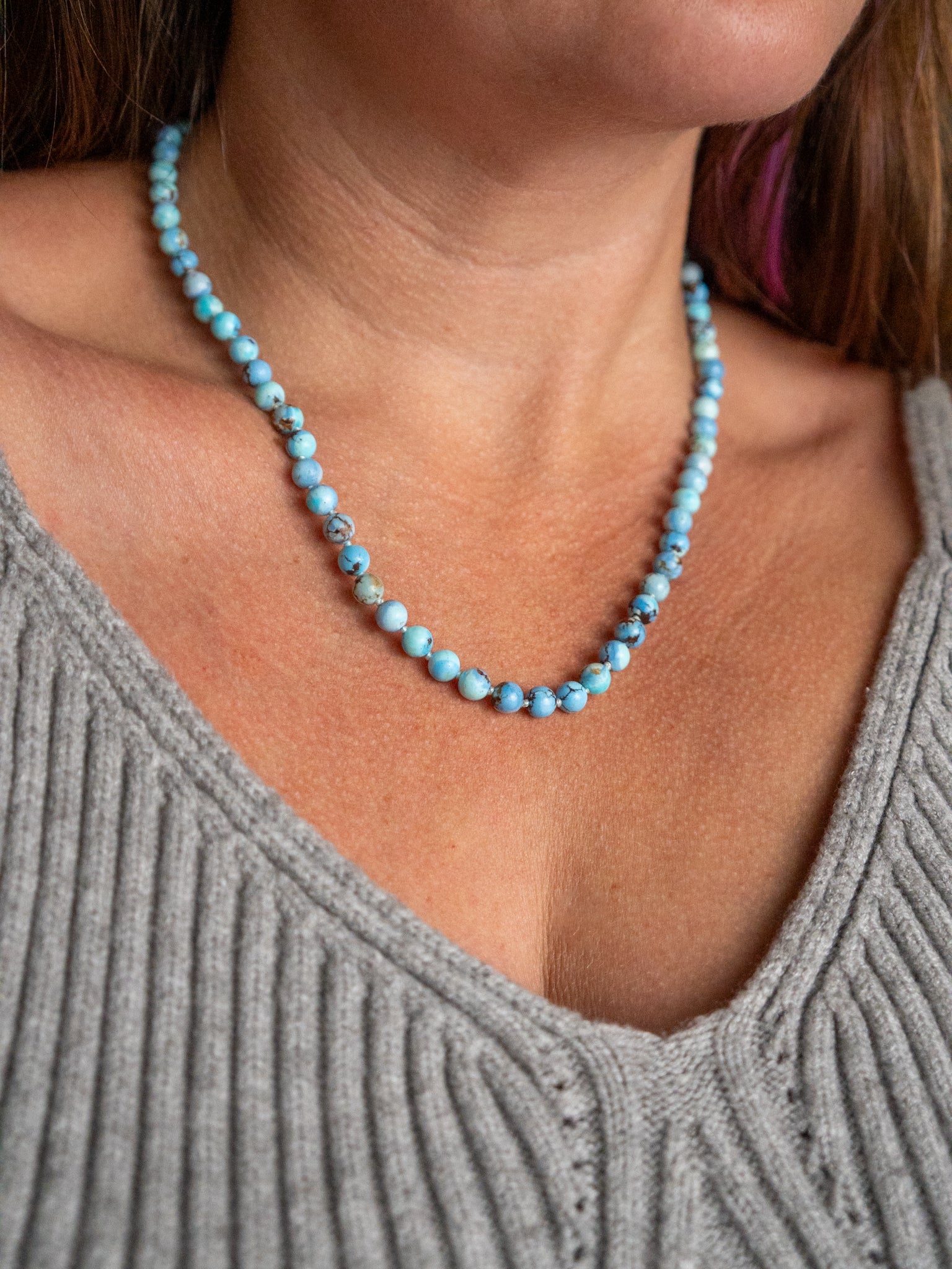 Kazakhstan turquoise beaded necklace worn at the collarbone with a gray ribbed top