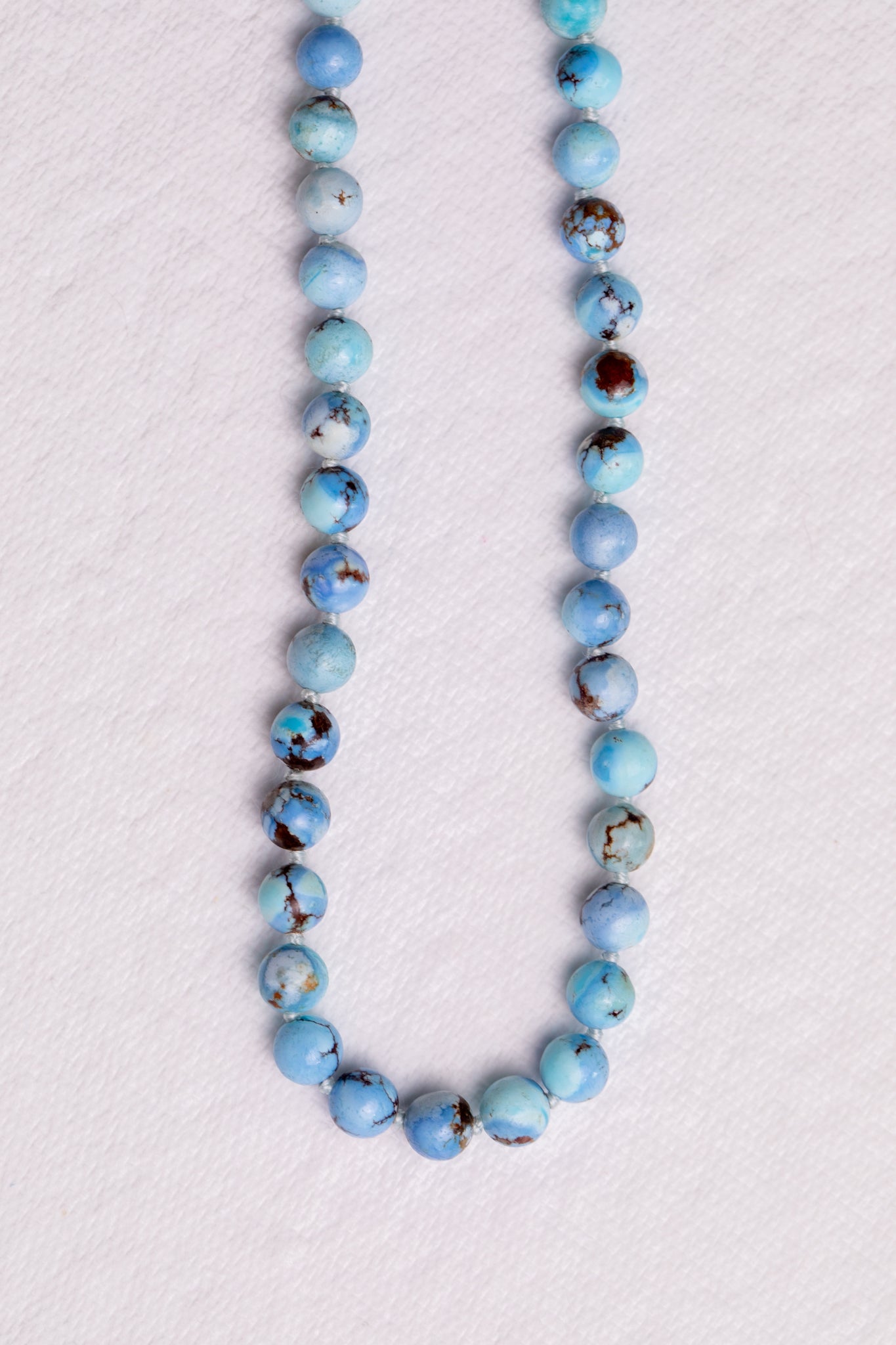 Handmade lavender turquoise knotted necklace showing natural color variation on white