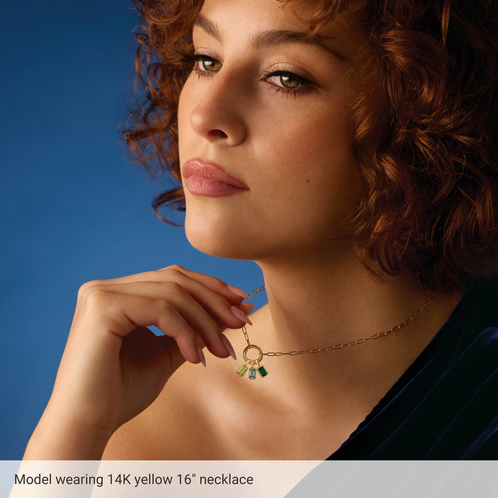 Woman wearing a 14K yellow gold necklace with green gemstones against a blue background