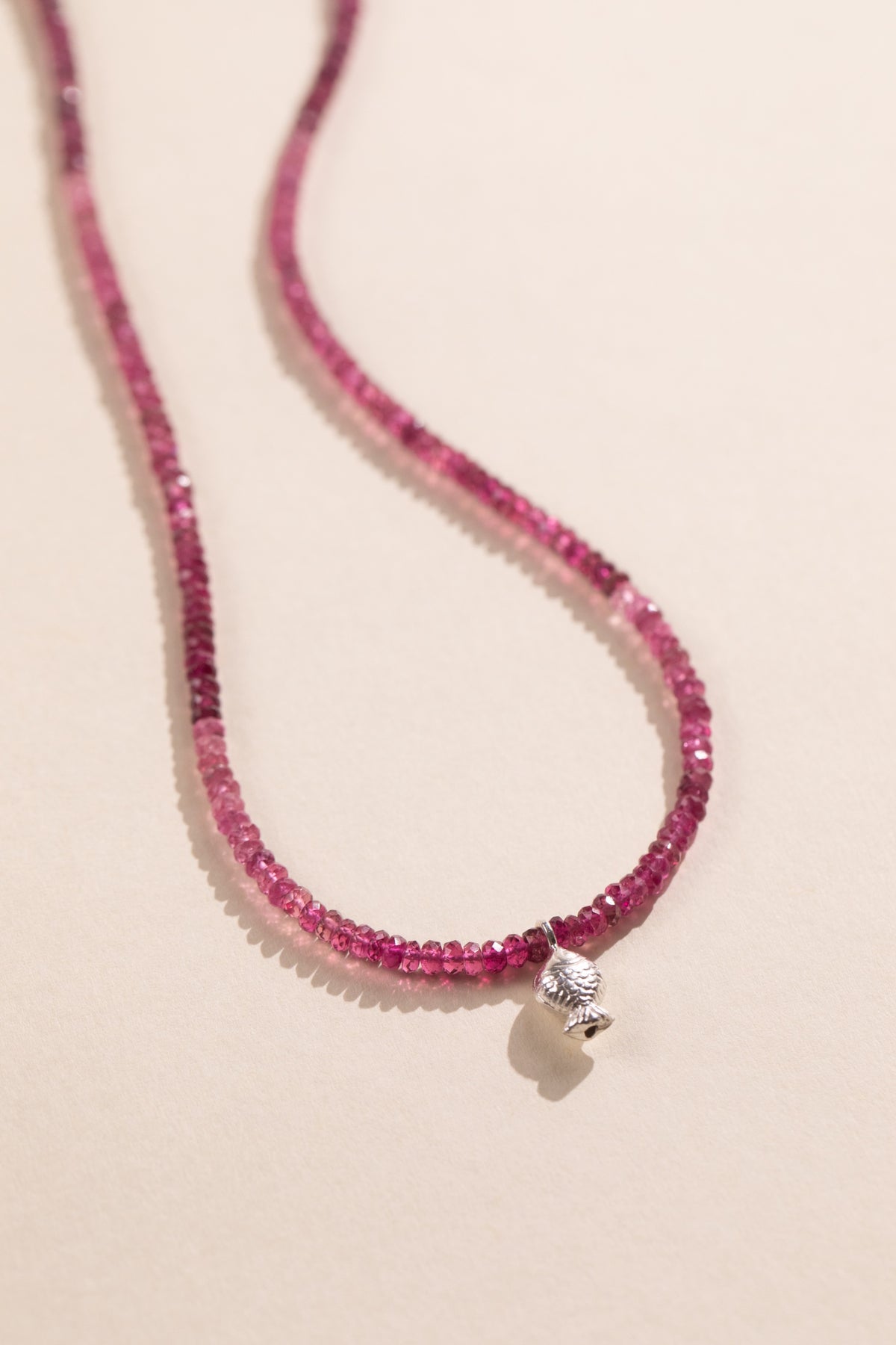 Faceted pink tourmaline strand shading from pale pink to raspberry with a sterling silver Worry Fish, view 2