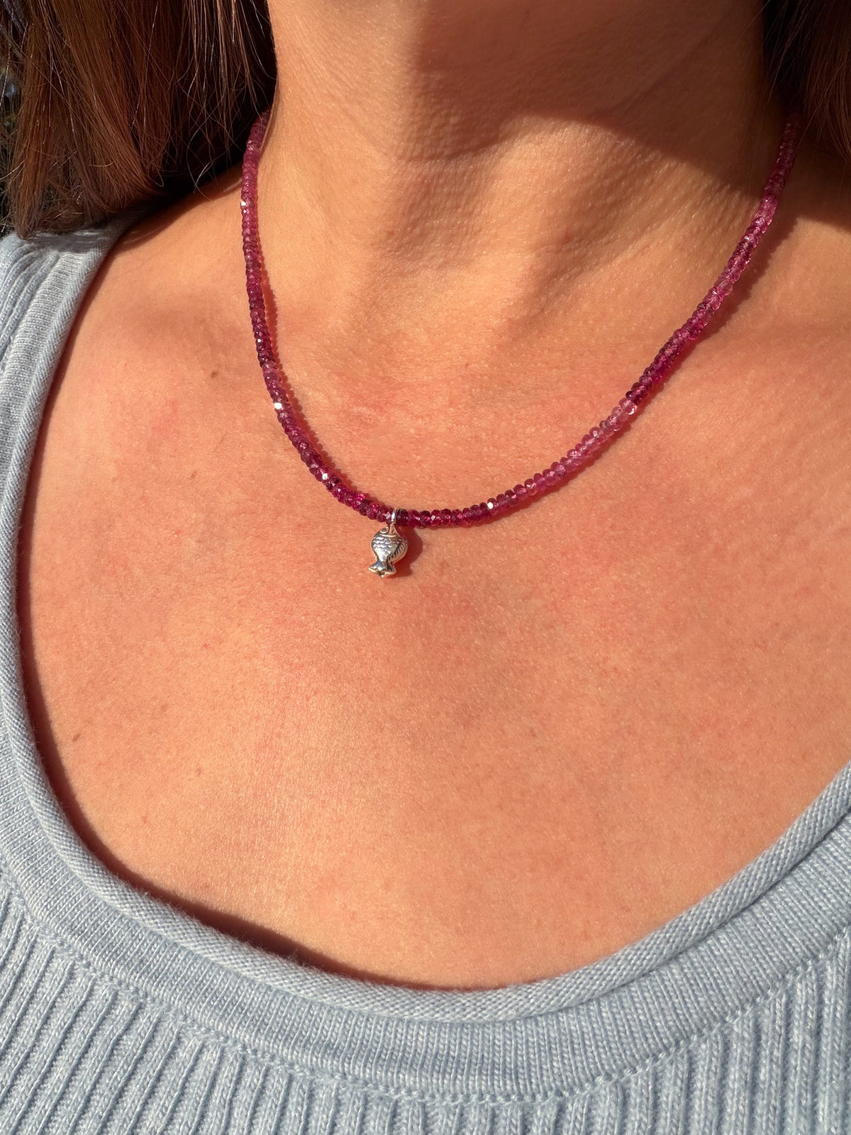Pink Tourmaline Worry Fish Necklace worn at the collarbone in sunlight