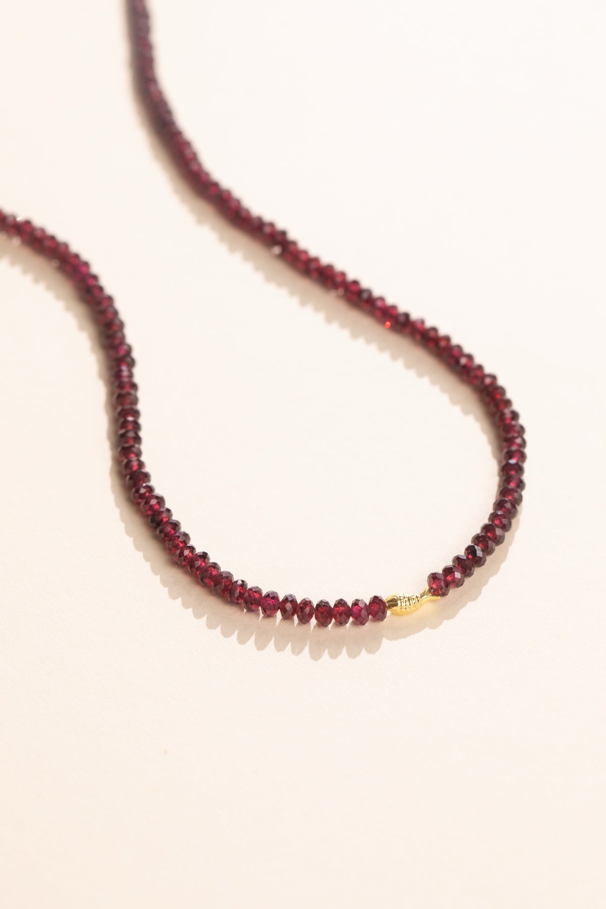 Faceted deep red pyrope garnet strand with a solid gold fish set in the strand, view 2