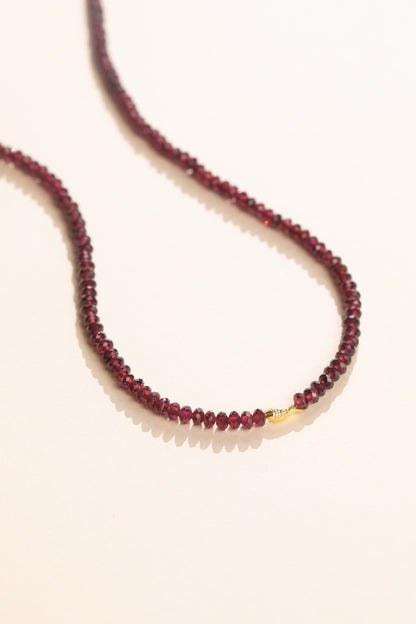 Faceted deep red pyrope garnet strand with a solid gold fish set in the strand, view 2