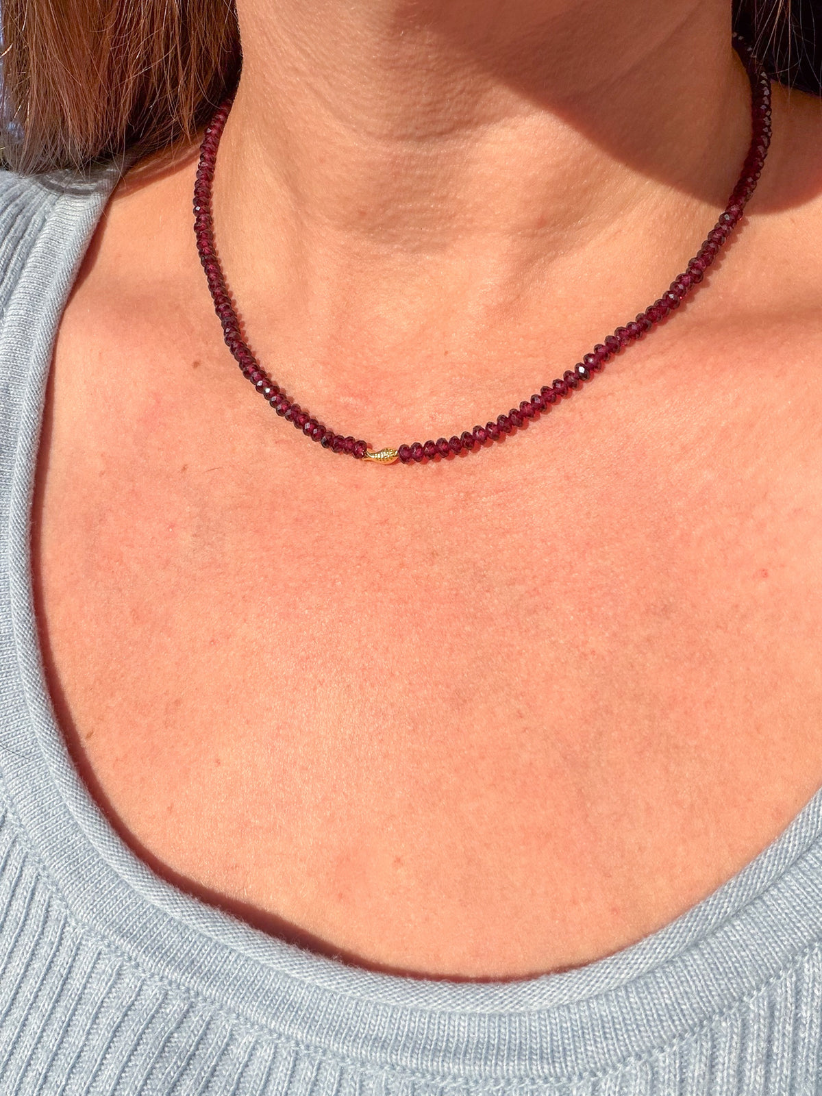 Pyrope Garnet Worry Fish Necklace worn at the base of the neck in sunlight