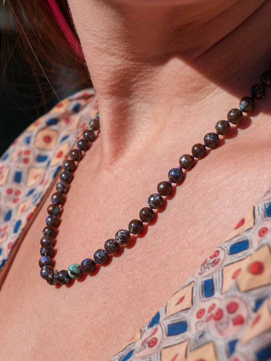 Close-up of a person wearing a beaded necklace with a patterned garment in the background real genuine australian boulder opal necklace 14k gold jewelry handmade
