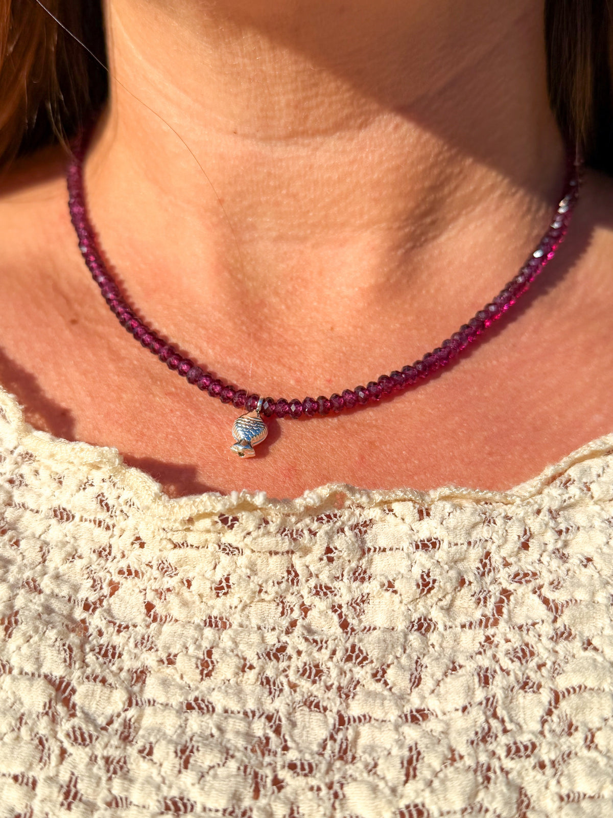 Rhodolite Garnet Worry Fish Necklace worn at the base of the neck with a cream lace top