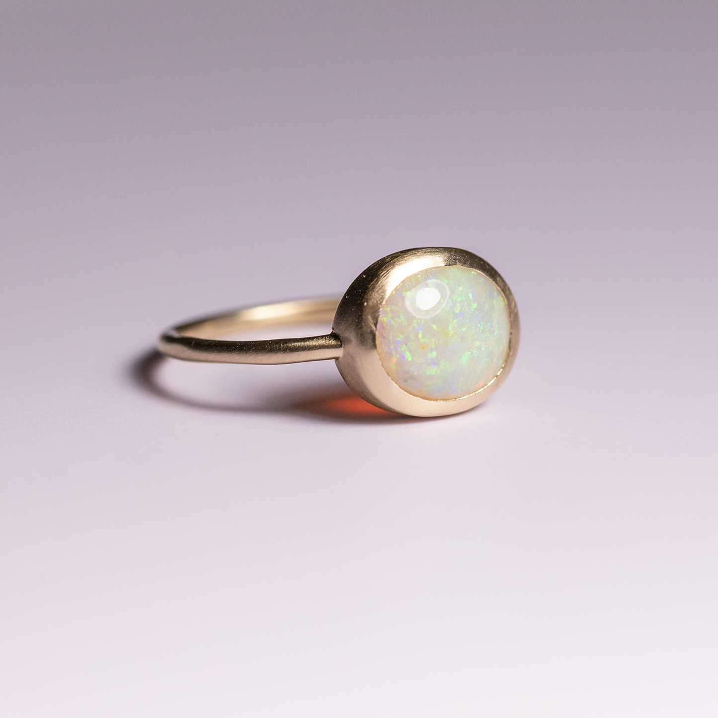 Gold ring with a round opal stone on a light purple background