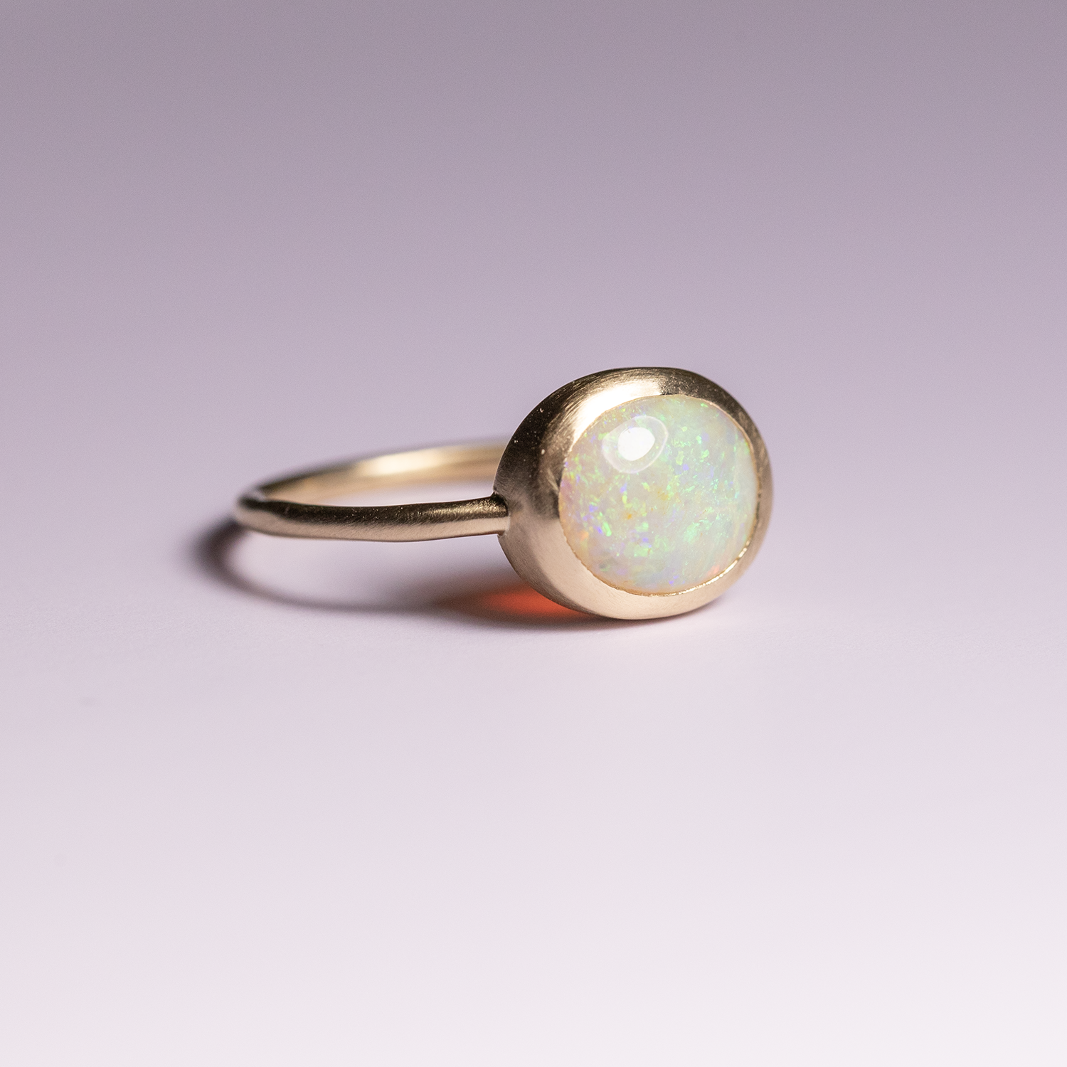 Gold ring with a round opal stone on a light purple background