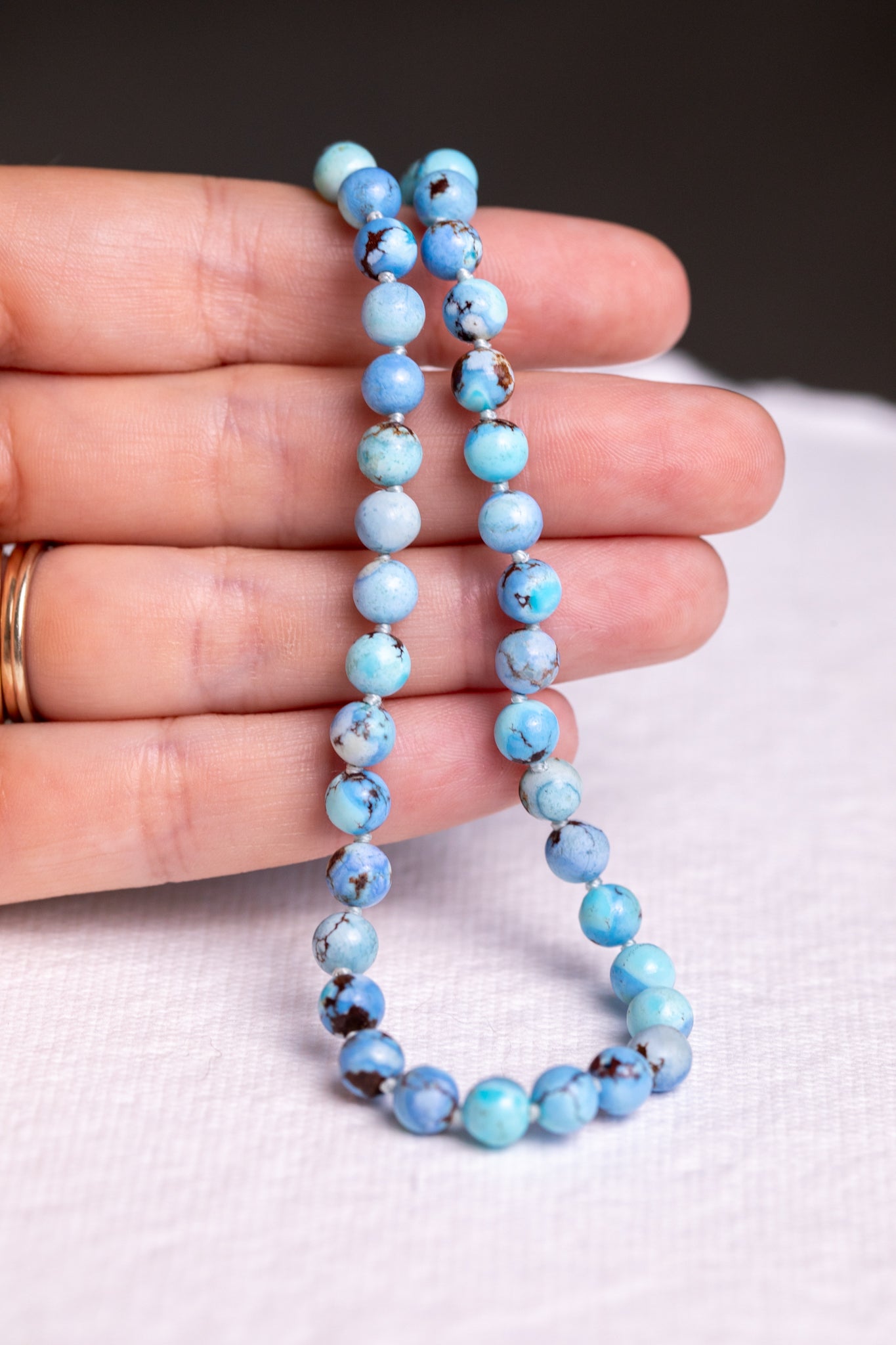 Silk knotted Kazakhstan turquoise strand draped over fingers showing knots between each bead