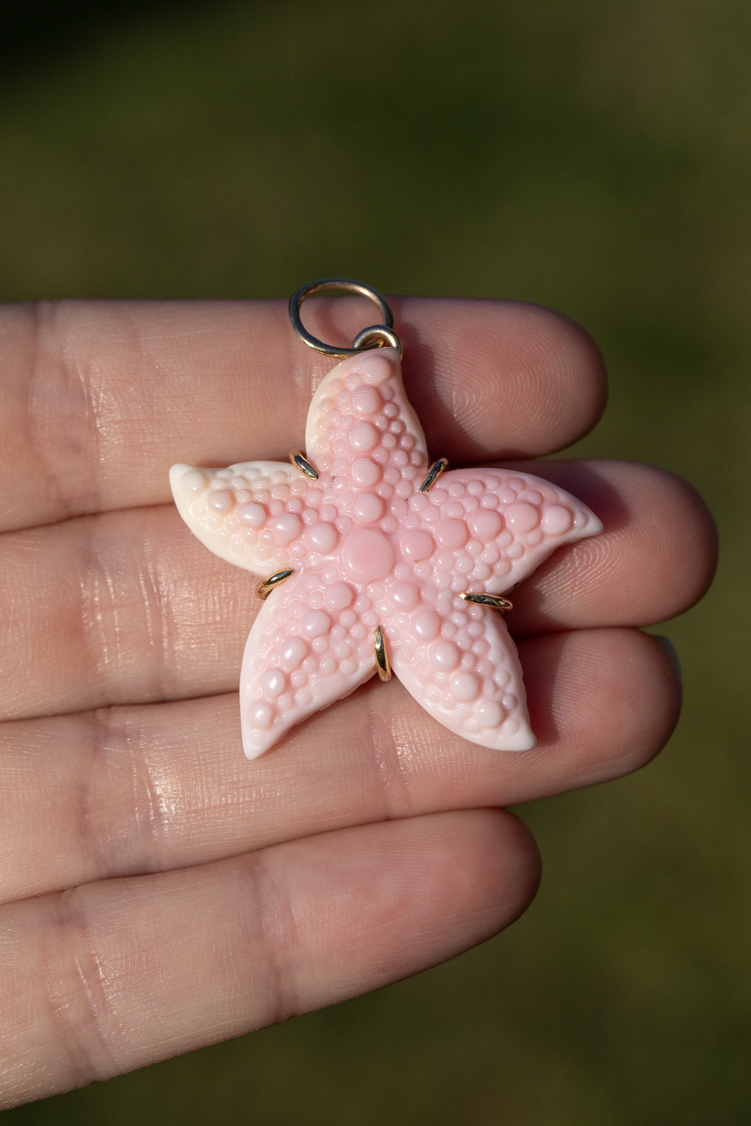 Pink starfish-shaped pendant held in a hand with a blurred green background