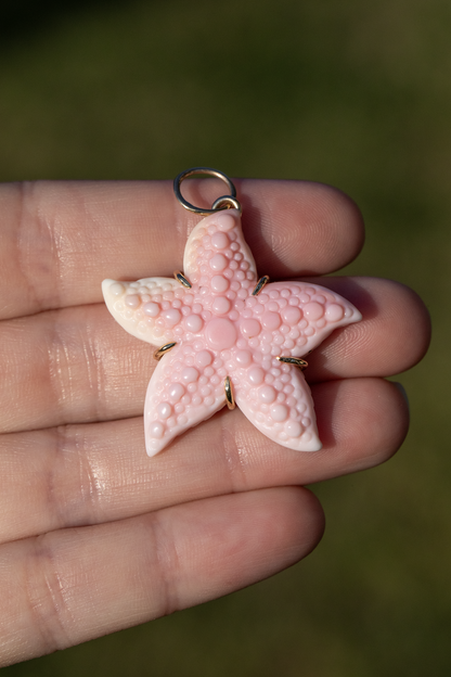 Pink starfish-shaped pendant held in a hand with a blurred green background
