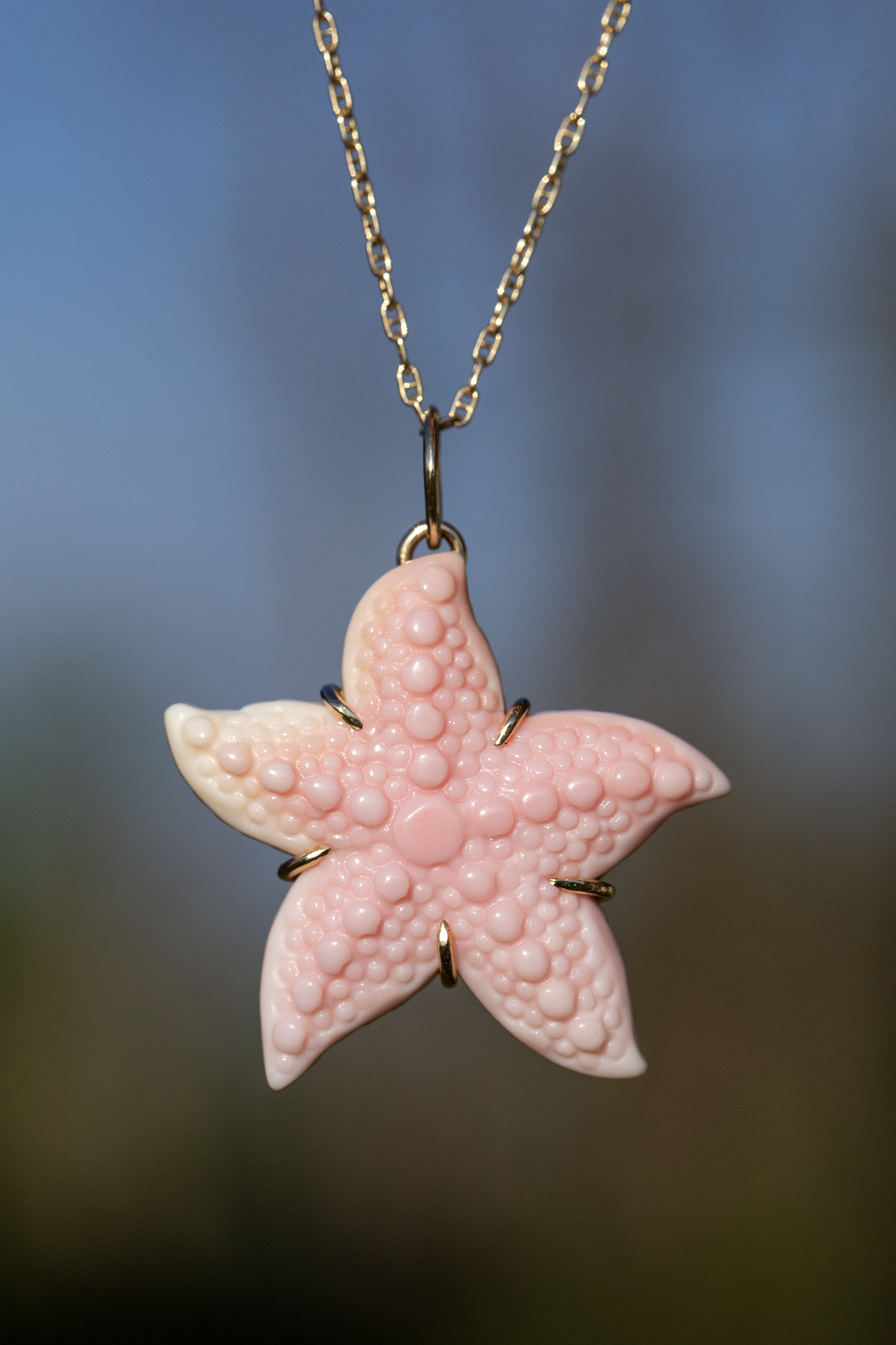 Pink starfish pendant on a chain against a blurred natural background