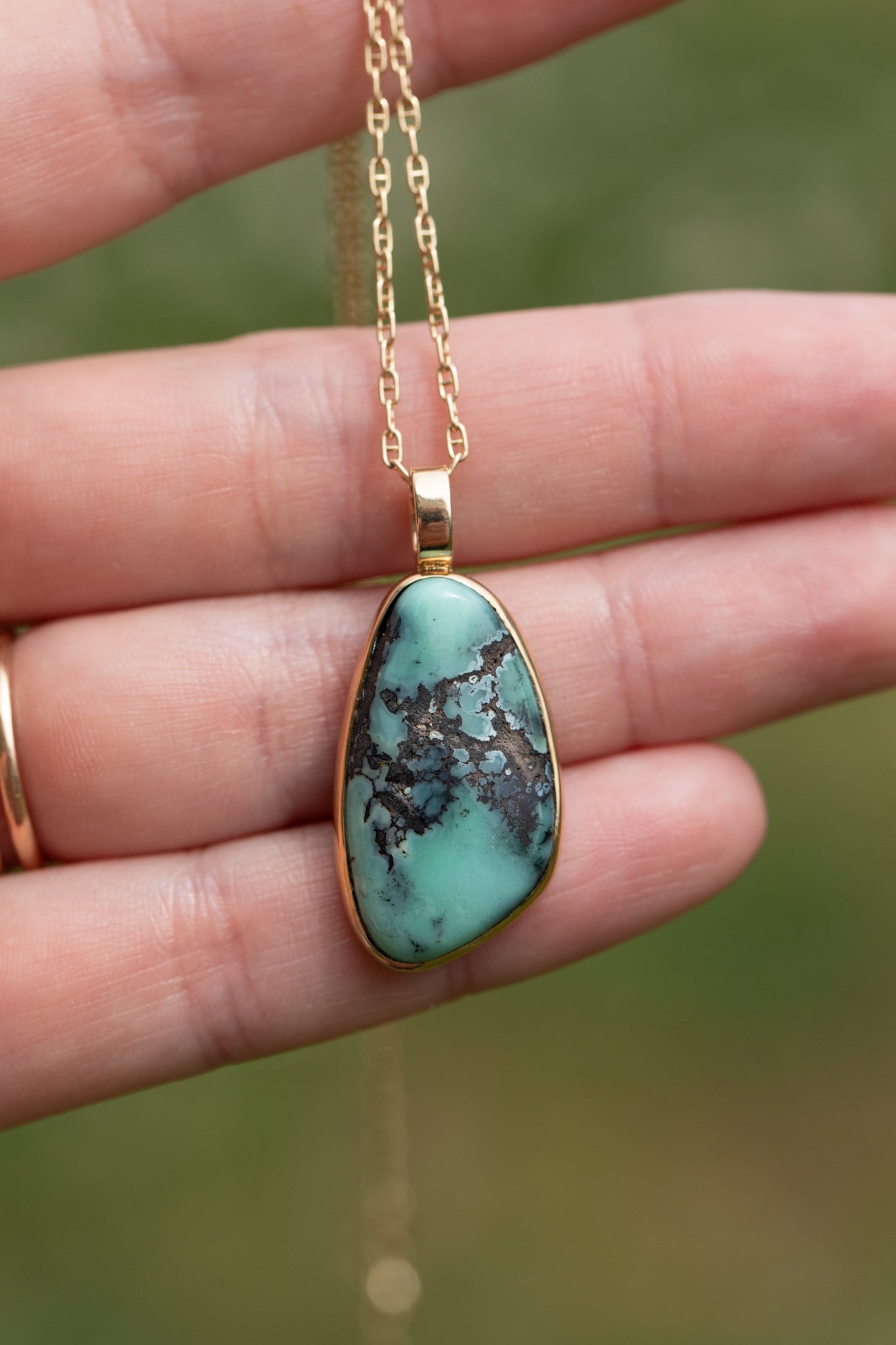 One of a kind variscite pendant held in a hand against a soft green background