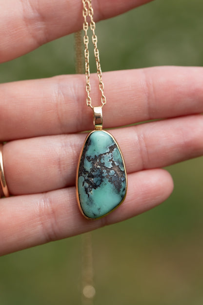 One of a kind variscite pendant held in a hand against a soft green background